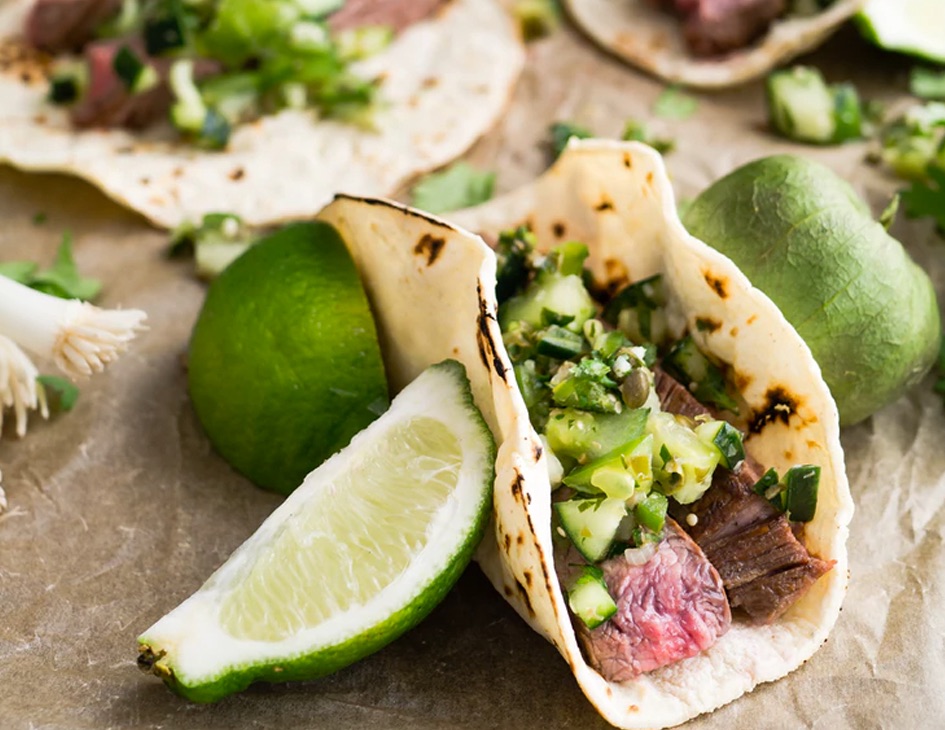 A taco stuffed with steak and pepper on top, with a slice of lime on the side
